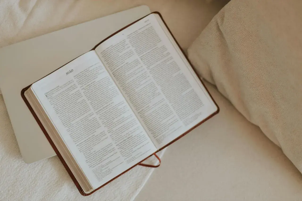 Otwarta Biblia, idealna do codziennej modlitwy. Na stronach widnieje tekst, a obok leży laptop.