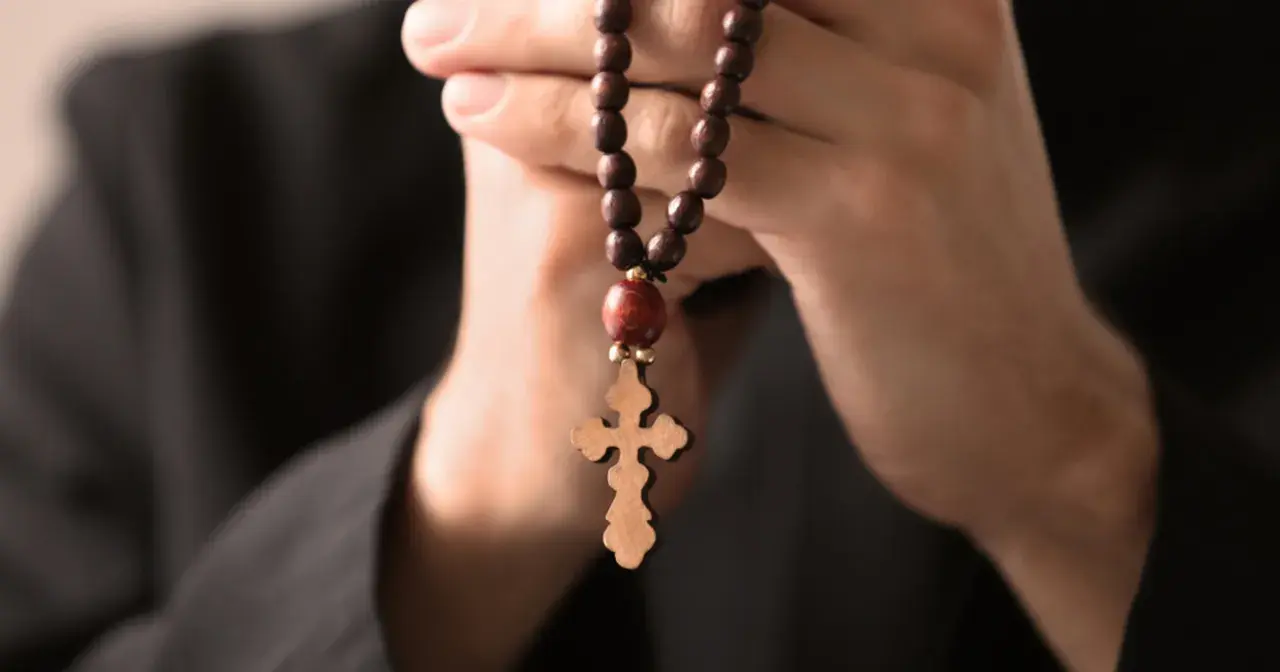 Dłonie trzymające drewniany różaniec z krzyżem, symbolizujące modlitwę do archanioła Rafała o uzdrowienie.