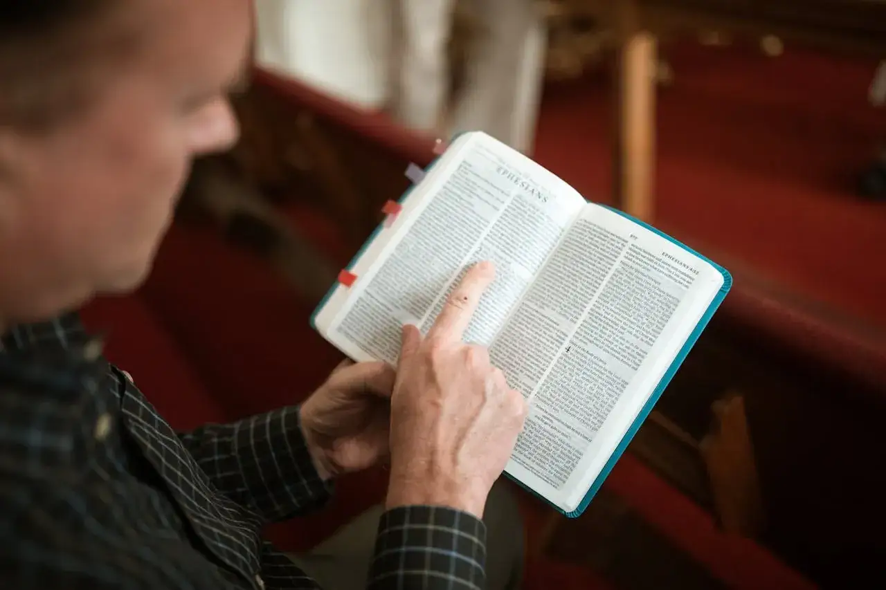Mężczyzna czyta Biblię, wskazując palcem na fragment z Listu do Filipian 4:13. Znajduje się w kościele, siedząc w ławce.