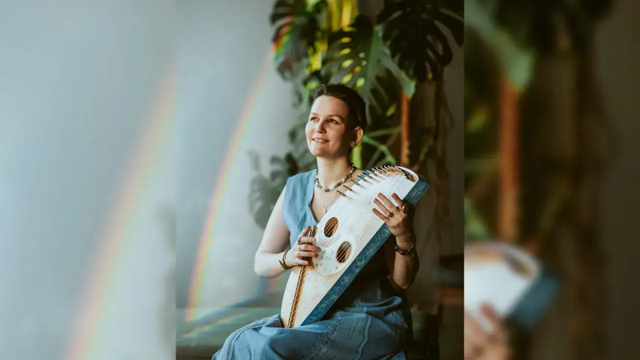 Kobieta z kantele, instrumentem strunowym, siedzi w otoczeniu roślin. Tęczę w tle można interpretować jako symbol nadziei, nawiązując do psalm 150.