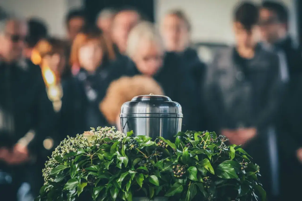 Urzna z kwiatami i liśćmi, otoczona żałobnikami. Pytanie, czy kremacja boli, pozostaje bez odpowiedzi.