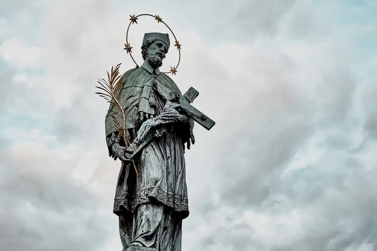 Kamienna rzeźba świętego Nepomucena z krzyżem i palmą, otoczona gwiazdami, na tle burzowego nieba.