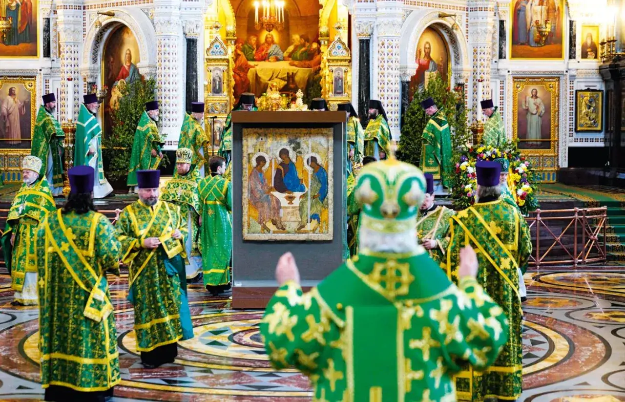 Uroczysta procesja duchownych w zielonych szatach w cerkwi. W centrum prawosławna ikona Trójcy Świętej.