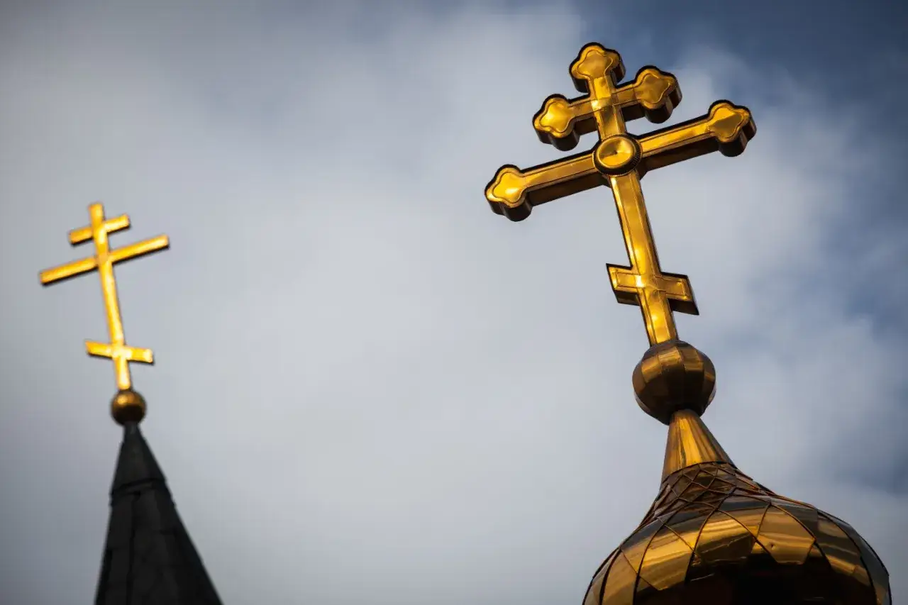 Złoty krzyż prawosławny lśni na tle nieba. Drugi, mniejszy krzyż prawosławny widoczny w oddali.