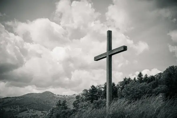 Drewniany krzyż na tle burzowych chmur, niczym biblijna góra, góruje nad zalesionym zboczem.